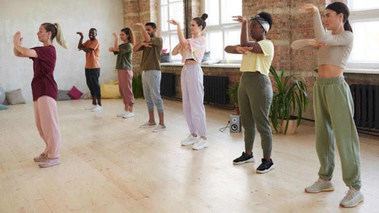 Group of young people standing and repeating the movements of the instructor in dance class in studio