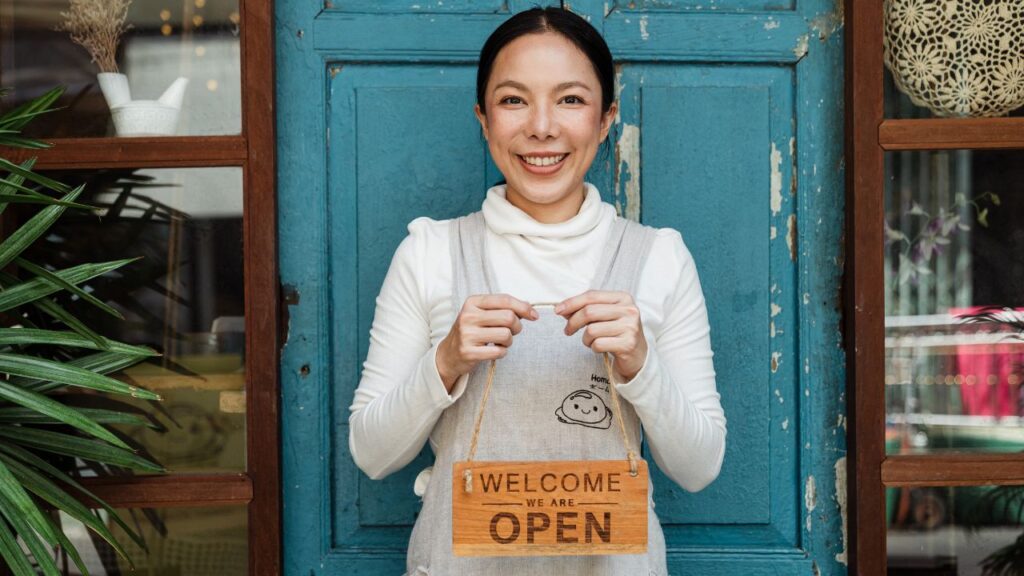 female cafe owner showing WELCOME WE ARE OPEN inscription