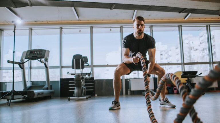 Fitness man working out with battle rope at gym