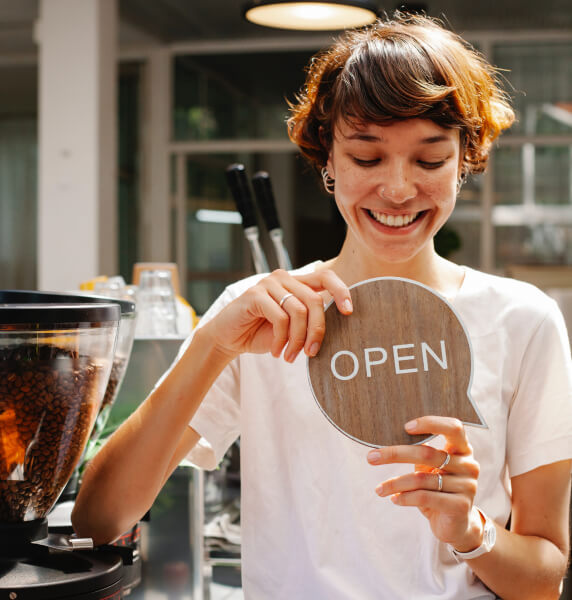 Smiling young woman standing in cafe with open sign